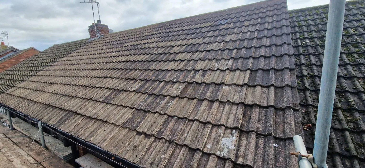 Wide view of a concrete tiled roof from scaffolding, with a chimney in the distance