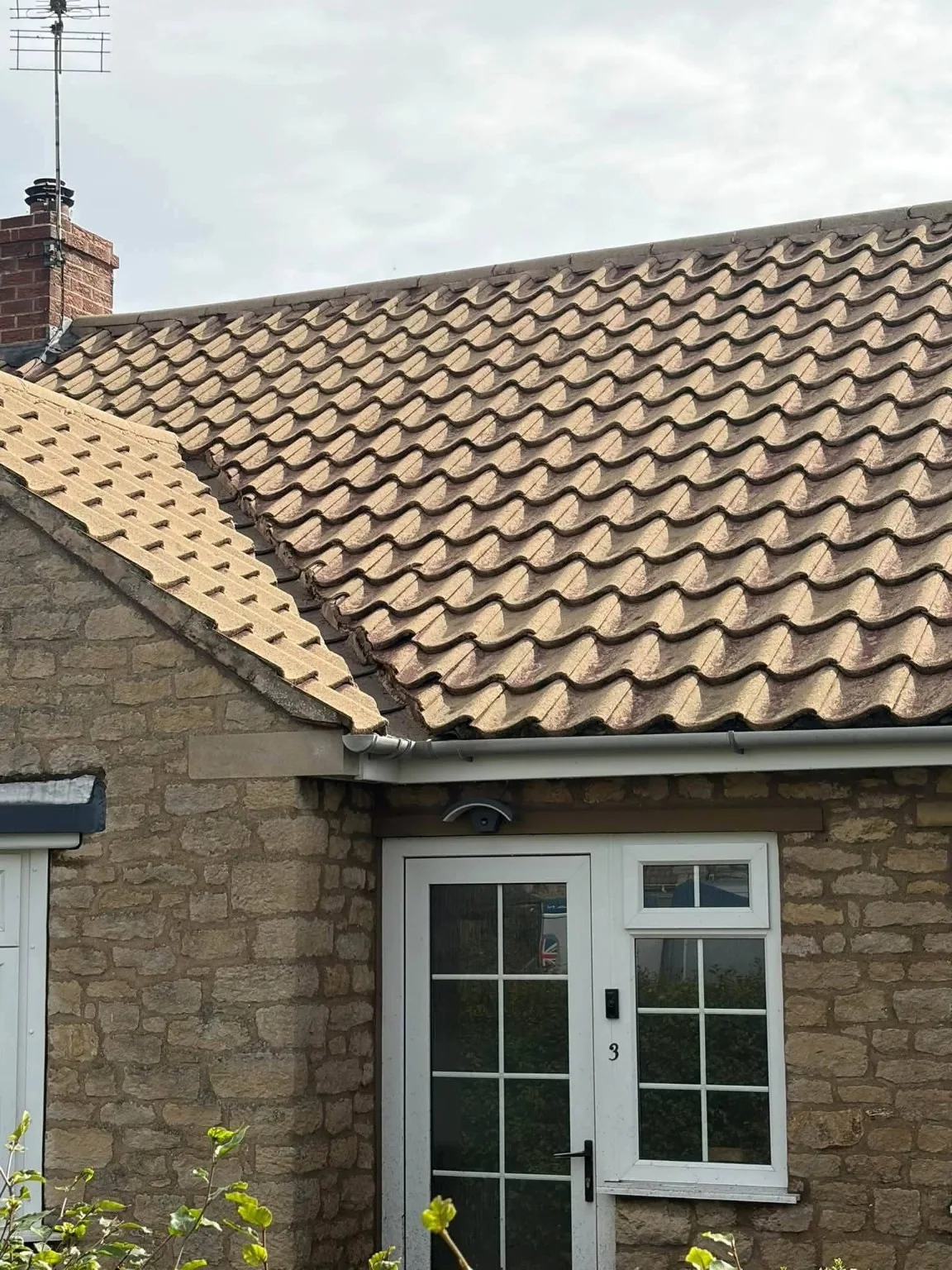 Light brown concrete tiled roof above a stone house with white windows